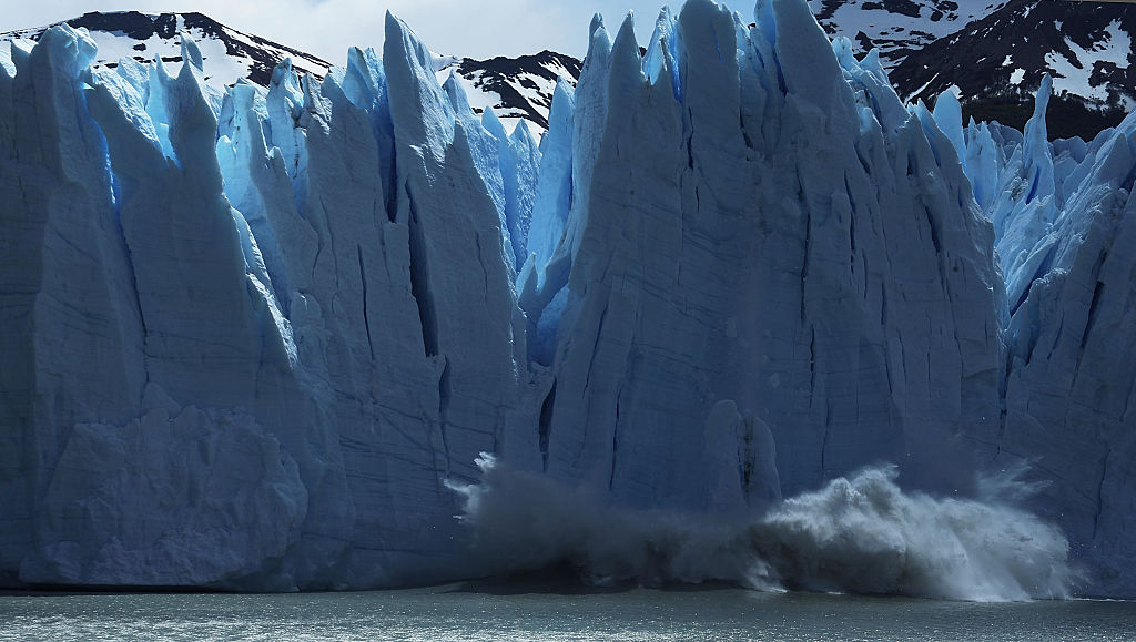 A giant spikey blue wall of glacial ice calves into the sea