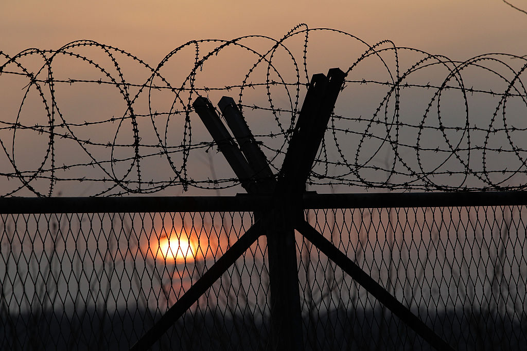 barbed wire and a wooden fence with a sunset behind it