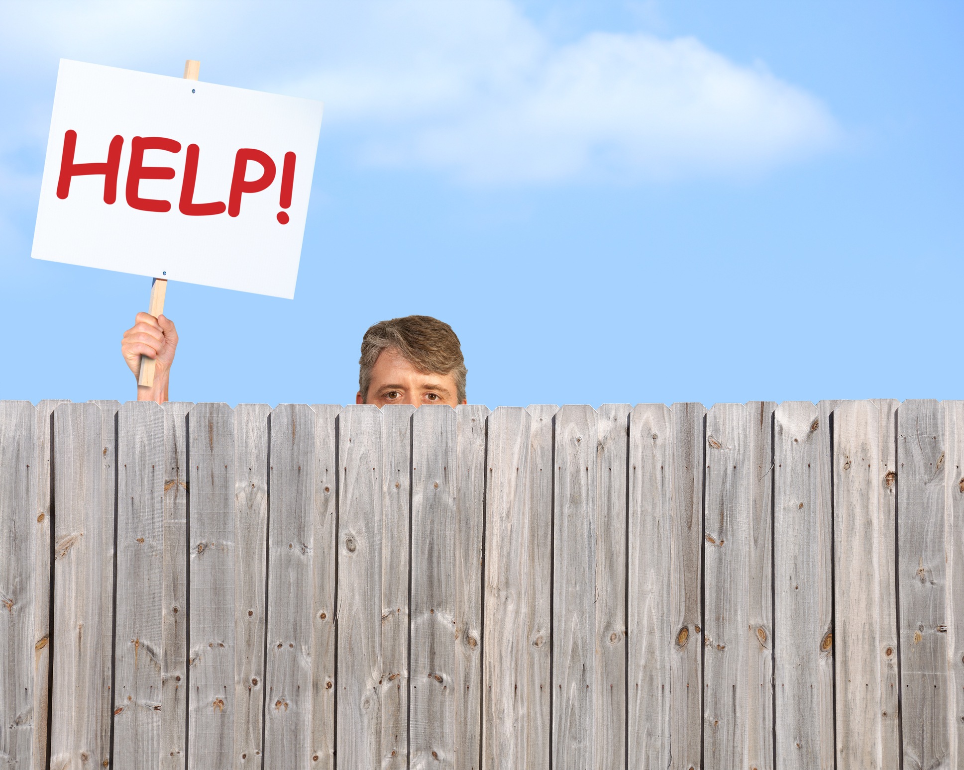 A man holding a HELP sign is peering over a fence desperate for help A man holding a HELP sign is peering over a fence desperate for help