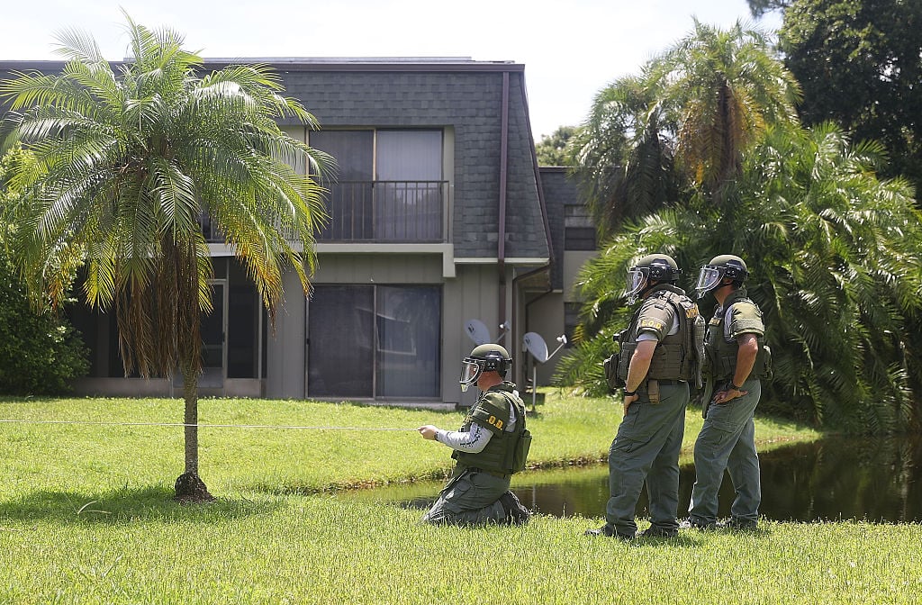 a bomb squad in green fatigues outside a gray apartment building with green grass and palm trees a bomb squad in green fatigues outside a gray apartment building with green grass and palm trees