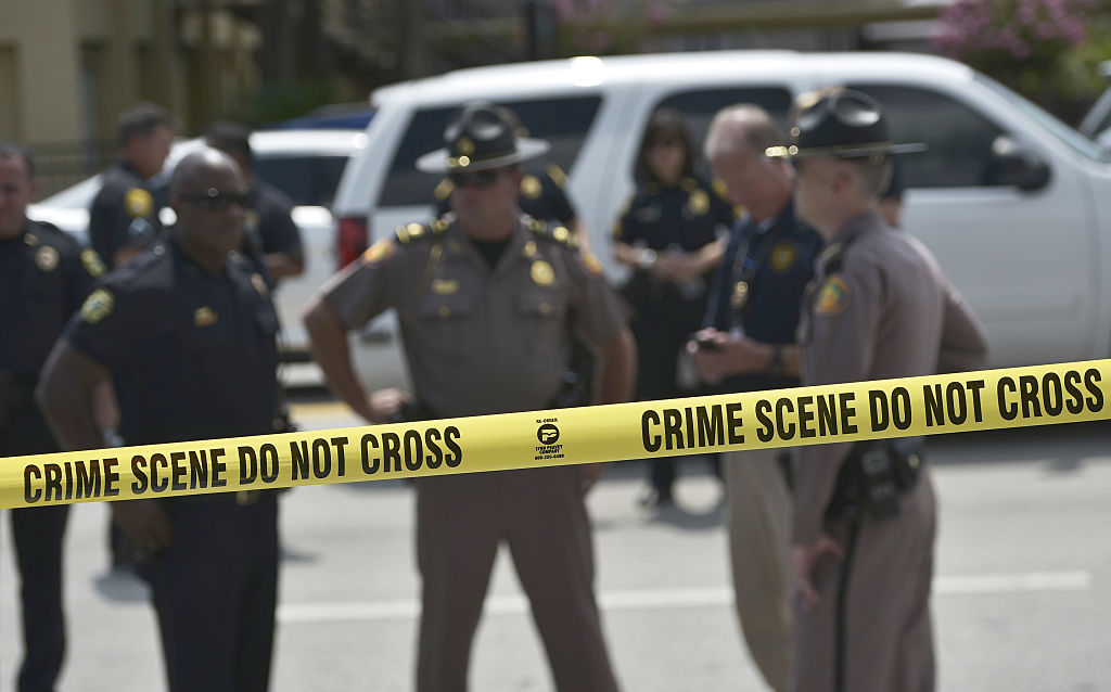 police officers in tan uniforms in front of white police cars behind yellow police tape police officers in tan uniforms in front of white police cars behind yellow police tape