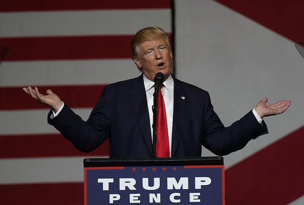 Donald Trump at a Trump-Pence podium in a blue suit and red tie against an American flag Donald Trump at a Trump-Pence podium in a blue suit and red tie against an American flag