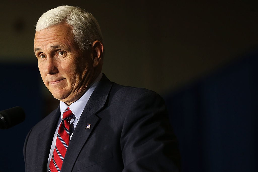 Mike Pence in a dark suit and red tie on a dark background