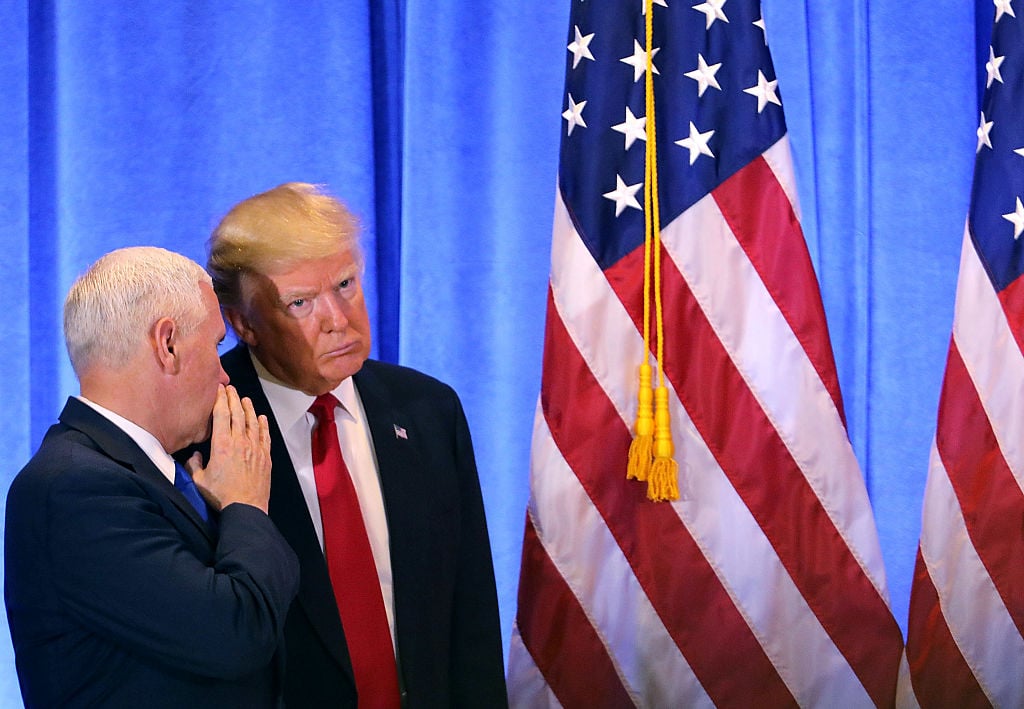 Donald Trump and Mike Pence whispering near an American flag
