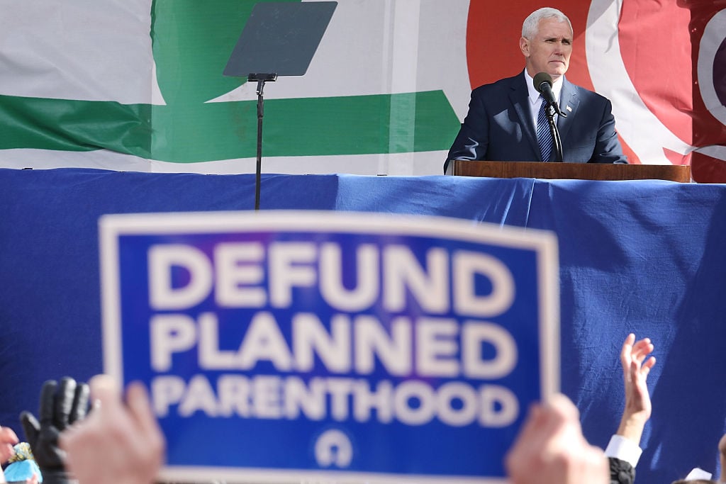 Mike Pence speaking with a blue and white defund planned parenthood sign in the foreground