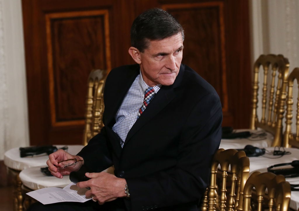 Michael Flynn in a dark suit with a piece of paper at a desk