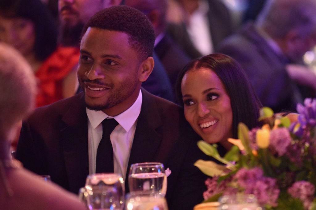 Nnamdi Asomugha and Kerry Washington smile and speak to other guests at a dinner table. 