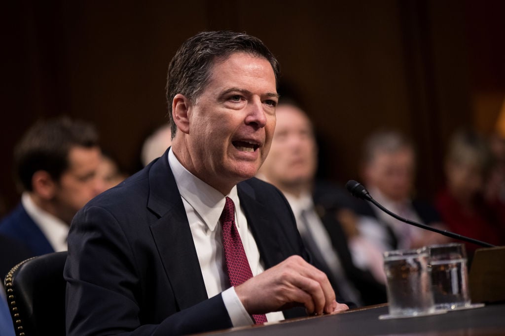 James Comey testifying in a dark suit and a red tie