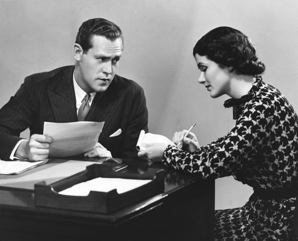 a black and white photo of a businessman with a secretary at a desk