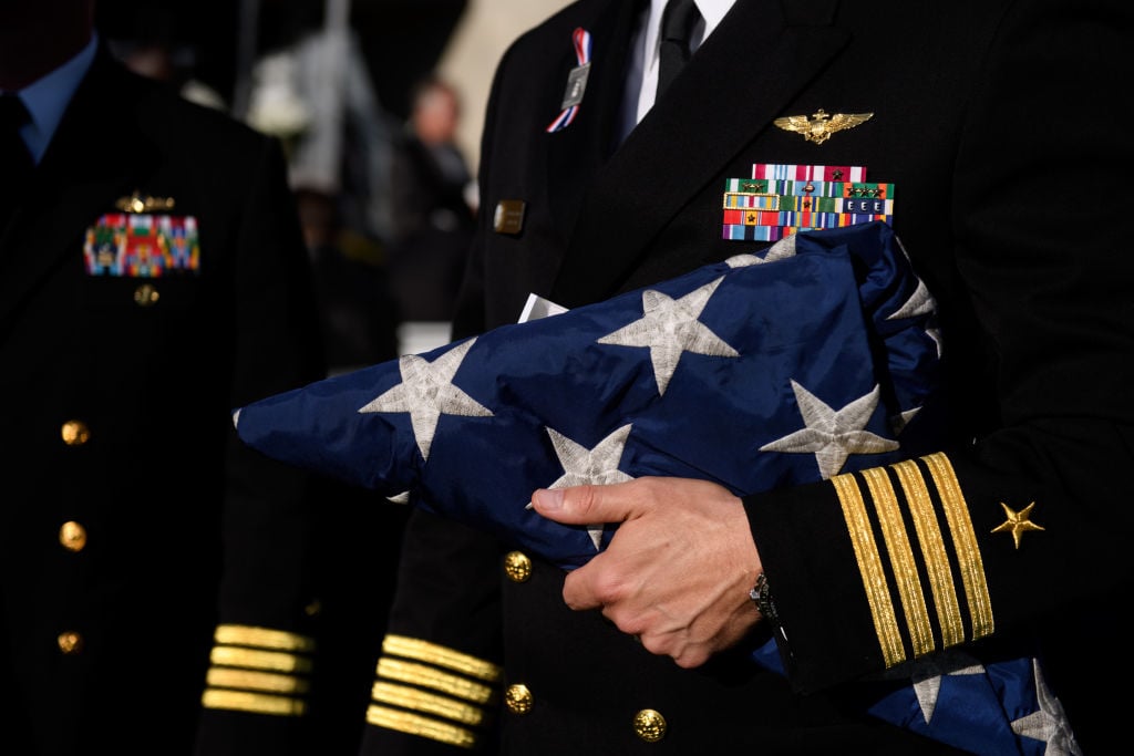 a hand in a blue military uniform with yellow stripes holding a folded American flag, stars out a hand in a blue military uniform with yellow stripes holding a folded American flag, stars out