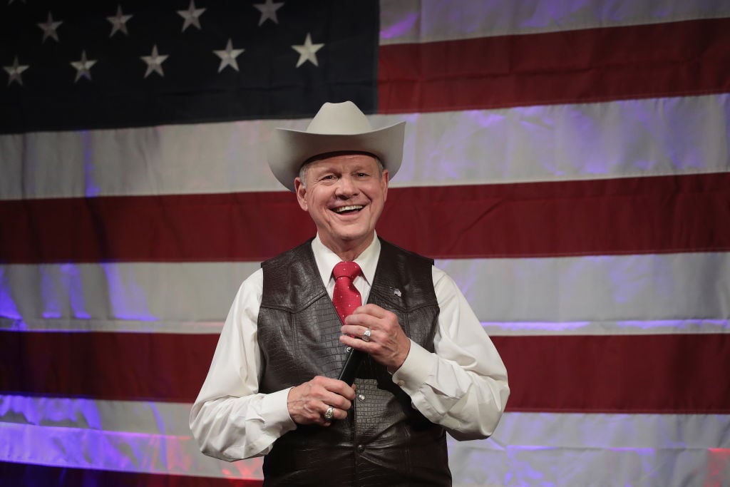 Roy Moore wears a leather vest and a cowboy hat, stands against an American flag Roy Moore wears a leather vest and a cowboy hat, stands against an American flag