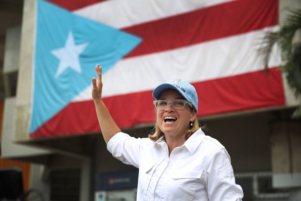San Juan mayor Carmen Yulin Cruz waves in a white shirt against the Puerto Rico flag San Juan mayor Carmen Yulin Cruz waves in a white shirt against the Puerto Rico flag