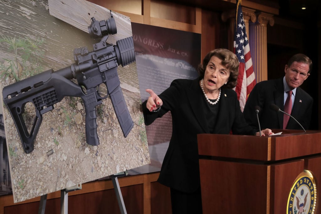 Sen Diane Feinstein in a dark suit points to a photo of a rifle with a bump stock Sen Diane Feinstein in a dark suit points to a photo of a rifle with a bump stock