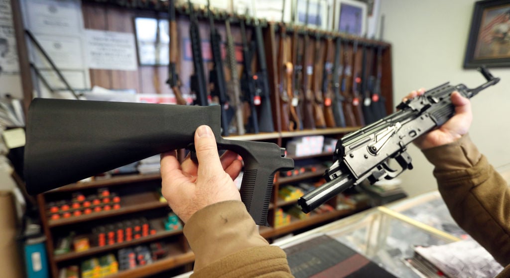 a man holds a bump stock rifle in front of a gun display a man holds a bump stock rifle in front of a gun display
