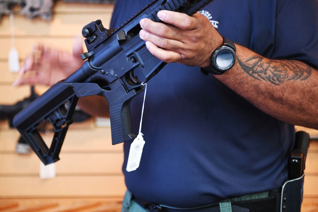 a salesman in a blue shirt shows off a bump stock on a rifle