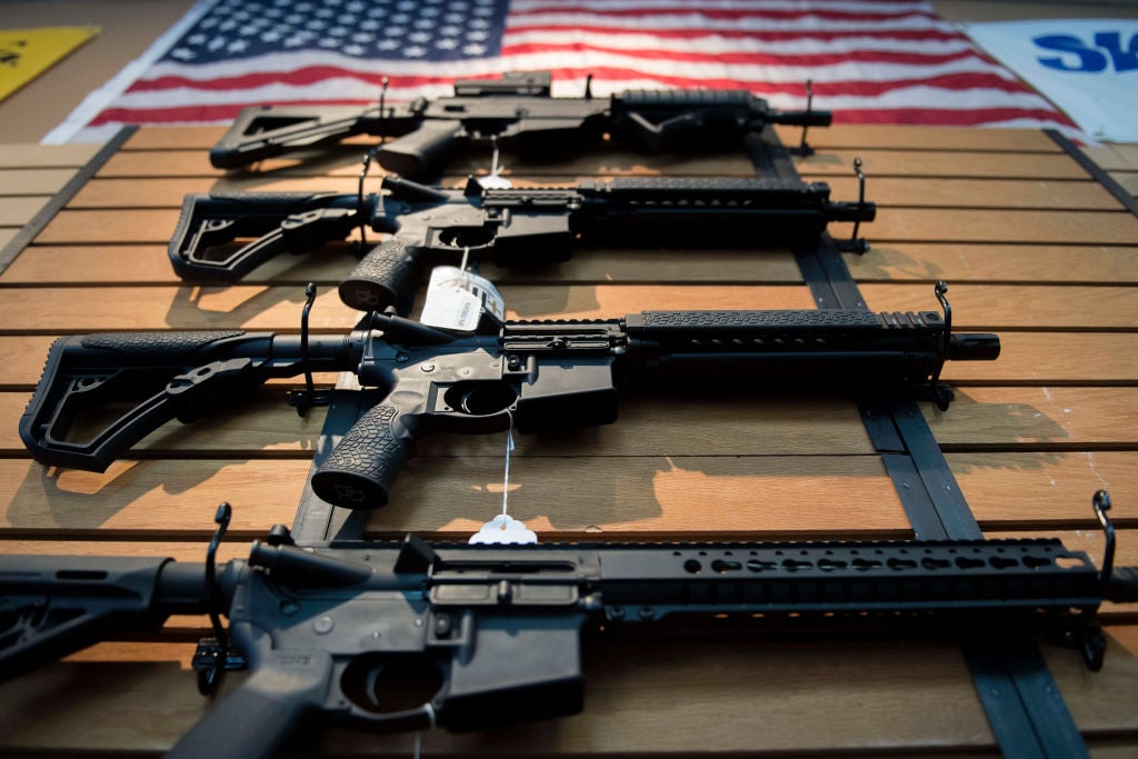 a display of assault rifles on a wood wall beneath an American flag