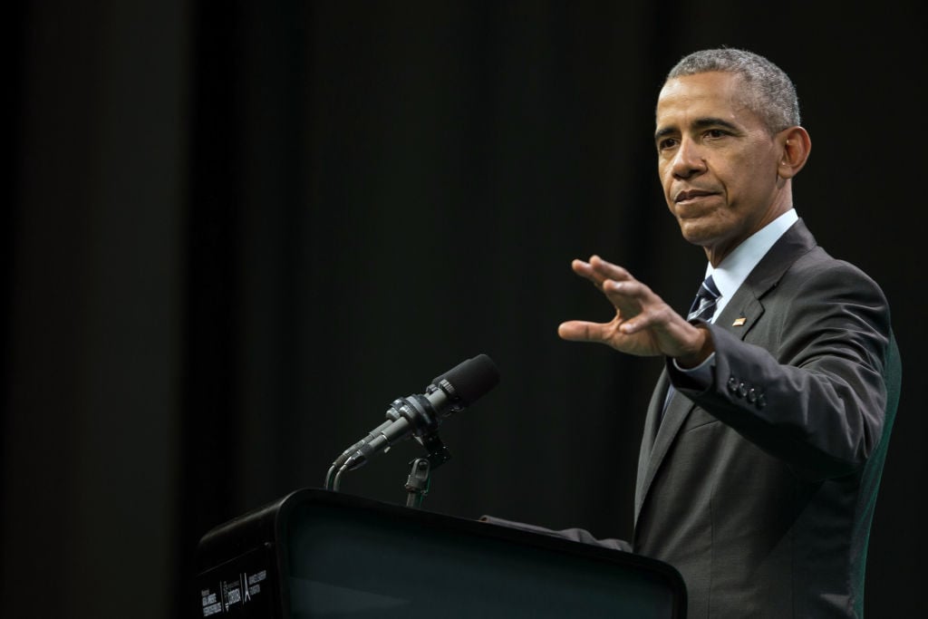 Barack Obama in a dark suit against a black background.