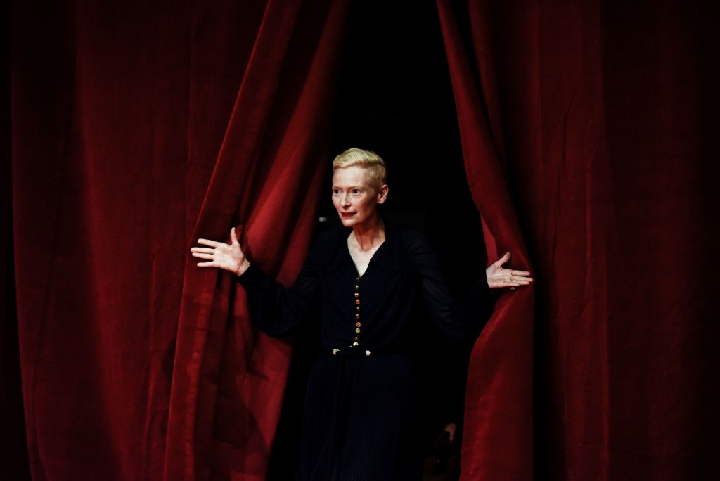 Tilda Swinton pulls back a red curtain Tilda Swinton pulls back a red curtain