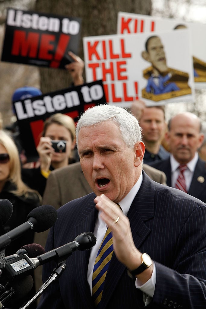 Mike Pence in a dark suit speaking against Tea party protest signs Mike Pence in a dark suit speaking against Tea party protest signs