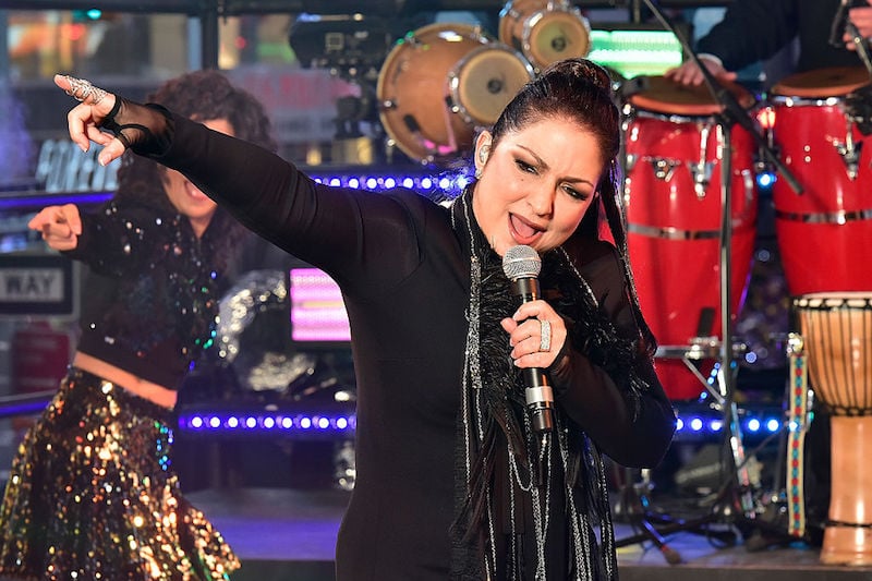 Gloria Estefan holding a microphone while performing on stage. Gloria Estefan holding a microphone while performing on stage.