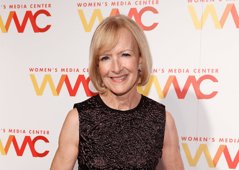 Judy Woodruff smiles and stands in a sequined gown at an event. 