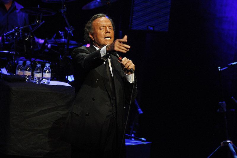 Julio Iglesias performing on stage while holding a microphone. Julio Iglesias performing on stage while holding a microphone.