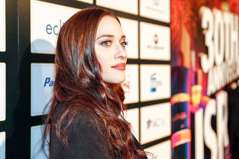 Kat Dennings smiling and looking forward in a black jacket.