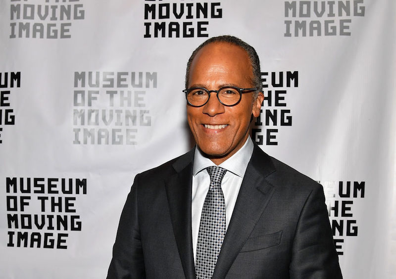 Lester Holt stands in a suit and glasses while smiling at a museum event. 