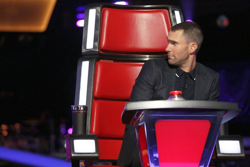 Adam Levine sits in a red chair on The Voice and looks to the side. Adam Levine sits in a red chair on The Voice and looks to the side.