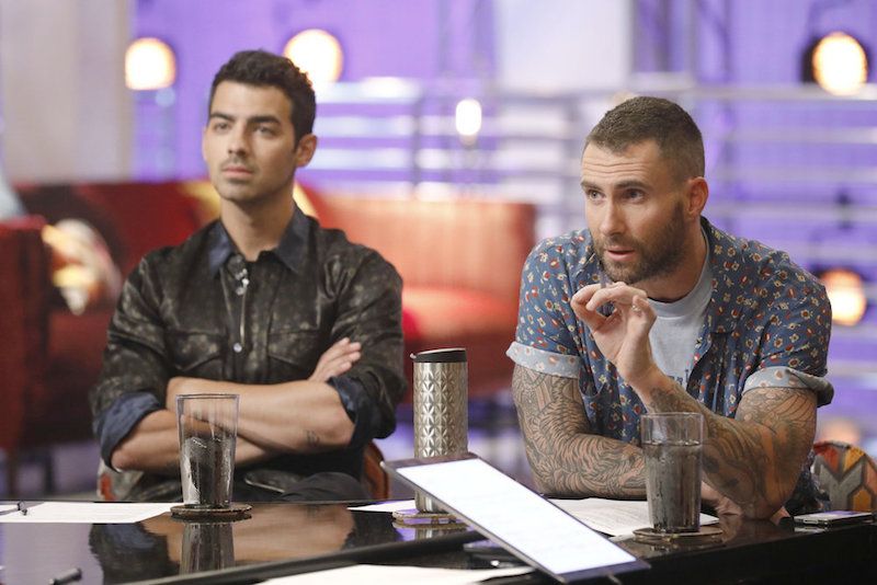Adam Levine and Joe jonas gesture with their hands while sitting next to each other
