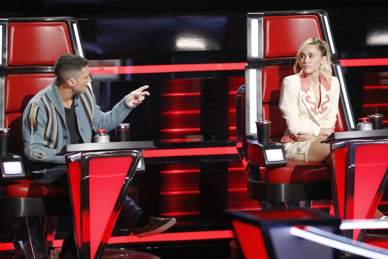 Adam Levine and Miley Cyrus sit next to each other in red chairs on The Voice