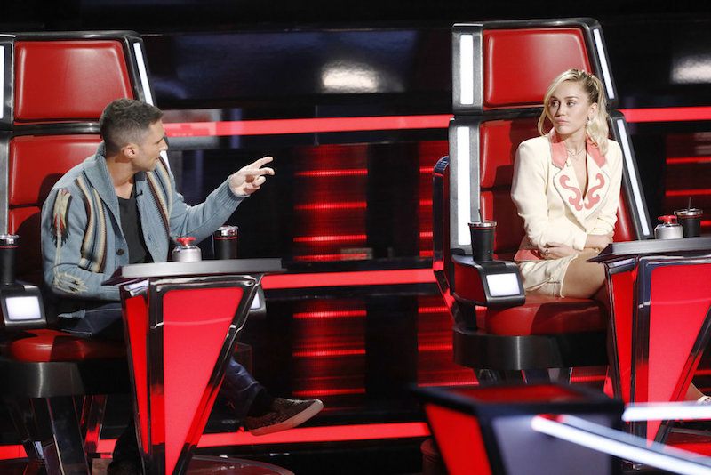 Adam Levine and Miley Cyrus sit next to each other in red chairs on The Voice Adam Levine and Miley Cyrus sit next to each other in red chairs on The Voice