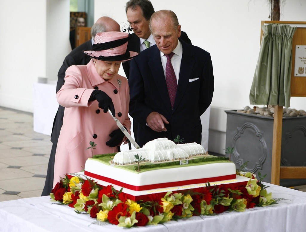 Queen Elizabeth II cuts a cake as Prince Philip looks on. 