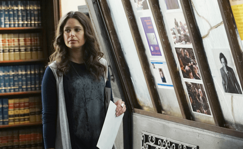 Quinn Perkins stands in front of a book shelf holding a sheet of paper. Quinn Perkins stands in front of a book shelf holding a sheet of paper.