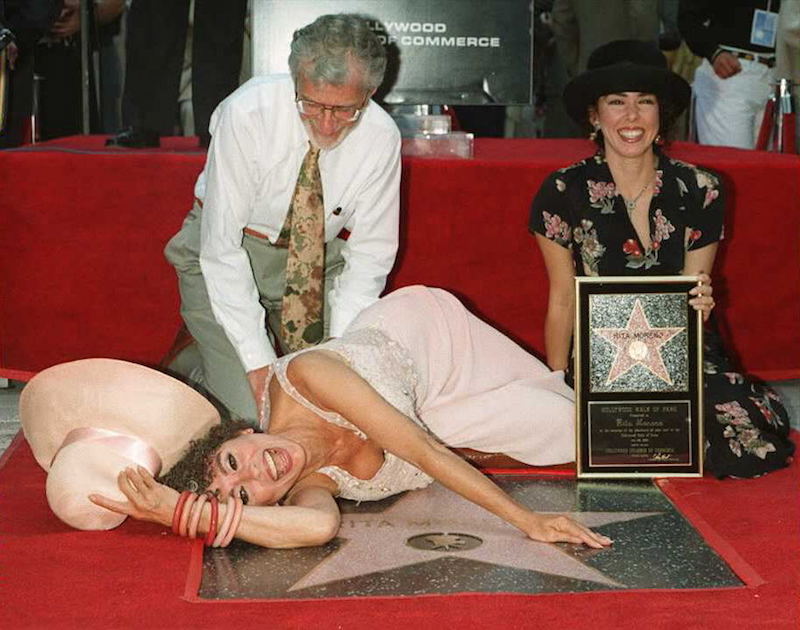 Rita Moreno lays on top of her star while her husband and daughter pose with her.