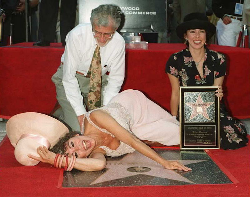Rita Moreno lays on top of her star while her husband and daughter pose with her. Rita Moreno lays on top of her star while her husband and daughter pose with her.