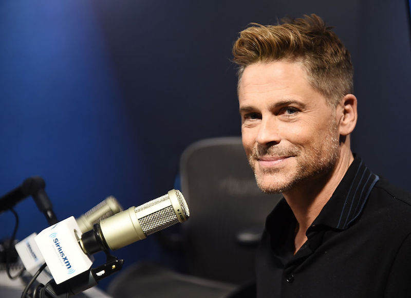 Rob Lowe sitting in front of a microphone and smiling.
