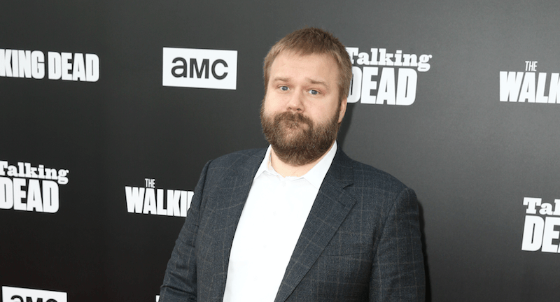 Robert Kirkman in a black plaid suit, stares straight ahead as he poses for photos at a premiere.