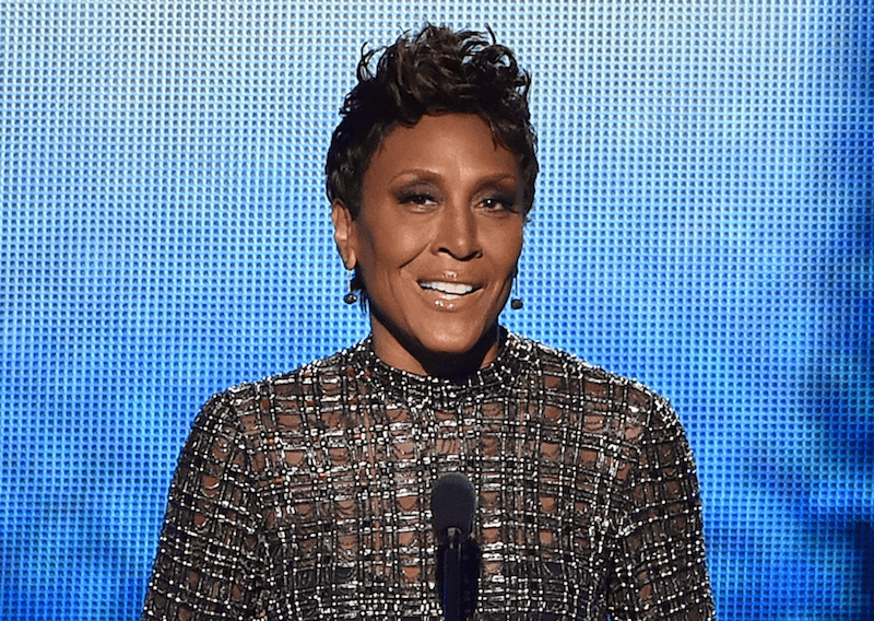Robin Roberts speaking on stage in front of a microphone in a sequined gown. 