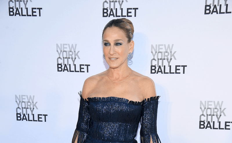 Sarah Jessica Parker standing in a blue fringe dress while holding a blue purse down at her side.