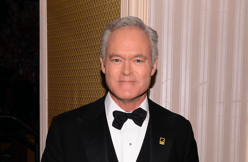 Scott Pelley smiles and stares straight ahead while wearing a black suit and bowtie. 