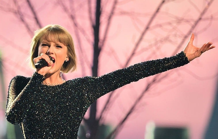 Singer Taylor Swift holds out her arm during a performance while holding a microphone and singing. 