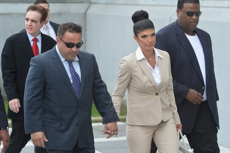 Joe and Teresa Giudice walking hand in hand on a sidewalk towards a courtroom.