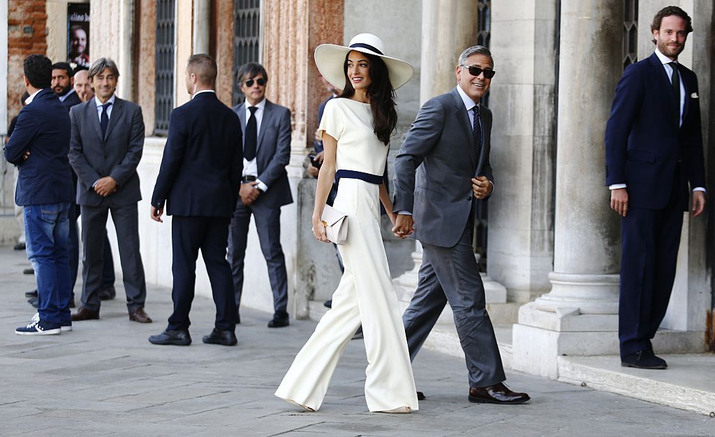 Amal and George Clooney walking while holding hands. 