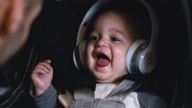 A baby with headphones on laughs in a car seat A baby with headphones on laughs in a car seat