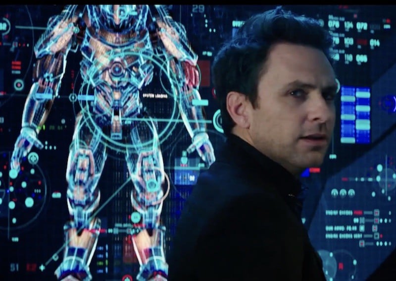 Charlie Day stands in front of a screen with an image of a robot Charlie Day stands in front of a screen with an image of a robot