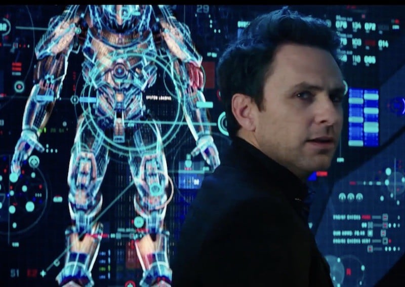 Charlie Day stands in front of a screen with an image of a robot