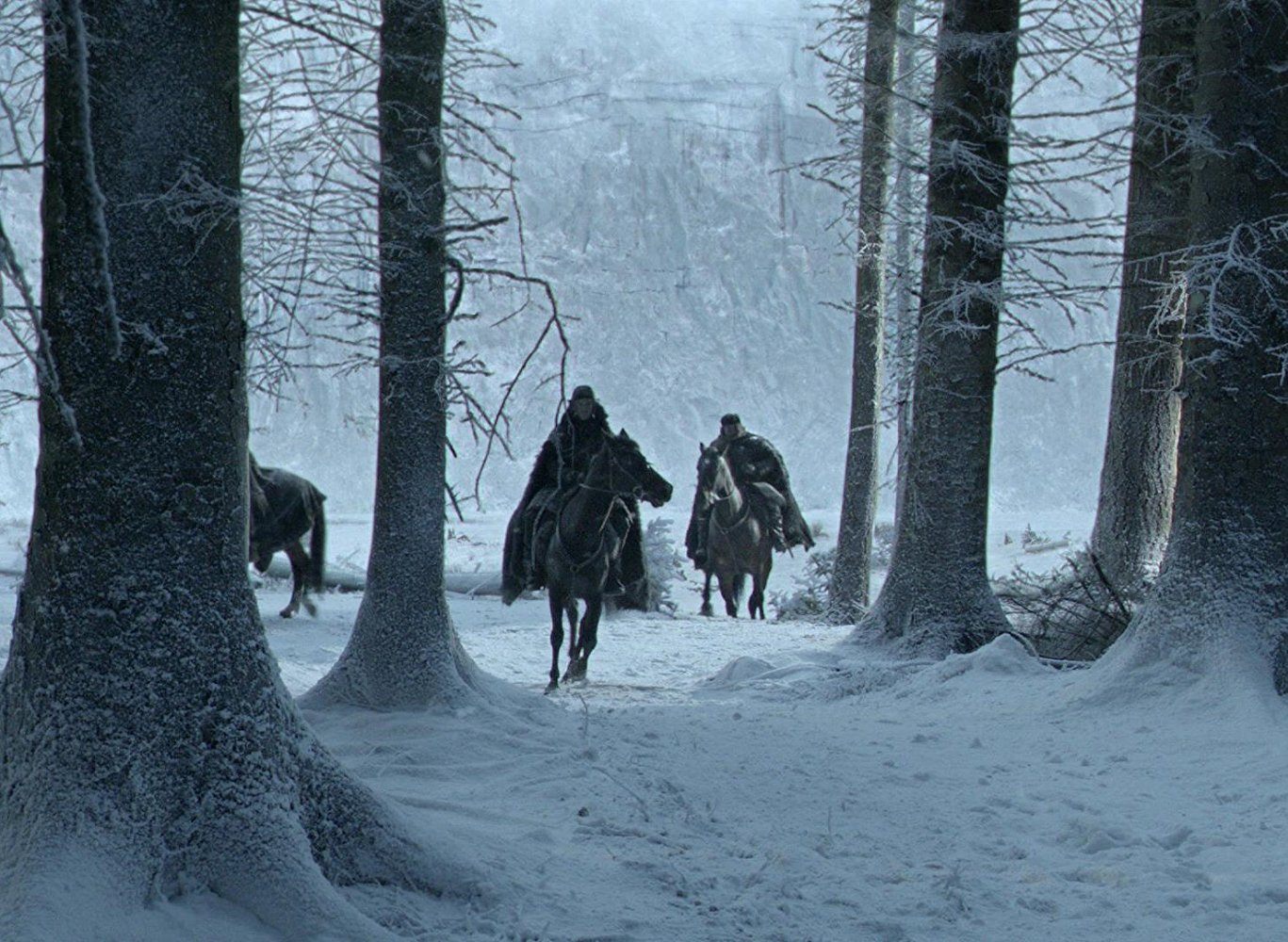 Men riding horses in the woods where snow has fallen.