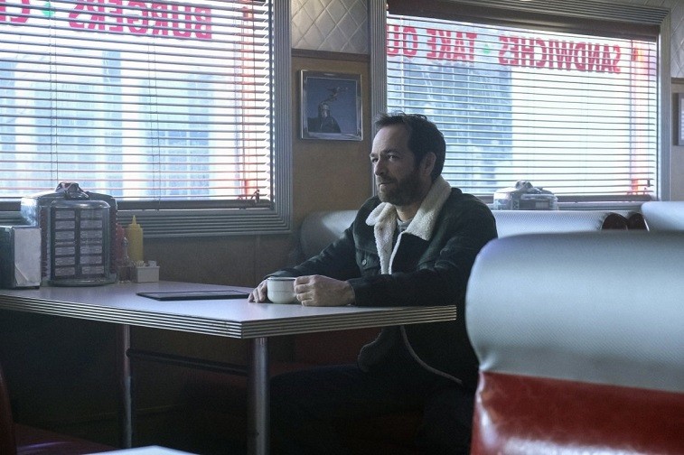 Luke Perry's Fred Andrews sits at a table holding a mug in Riverdale