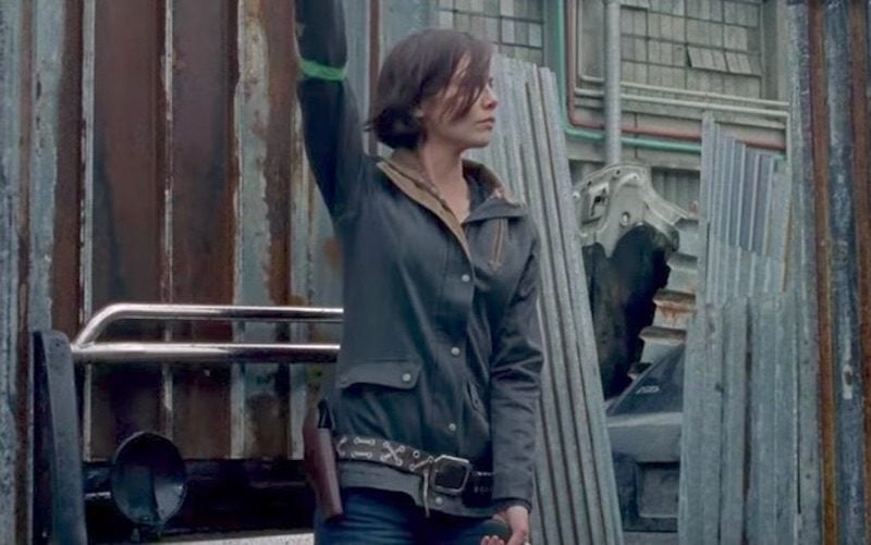 Maggie lifts her arm while standing in front of a wall